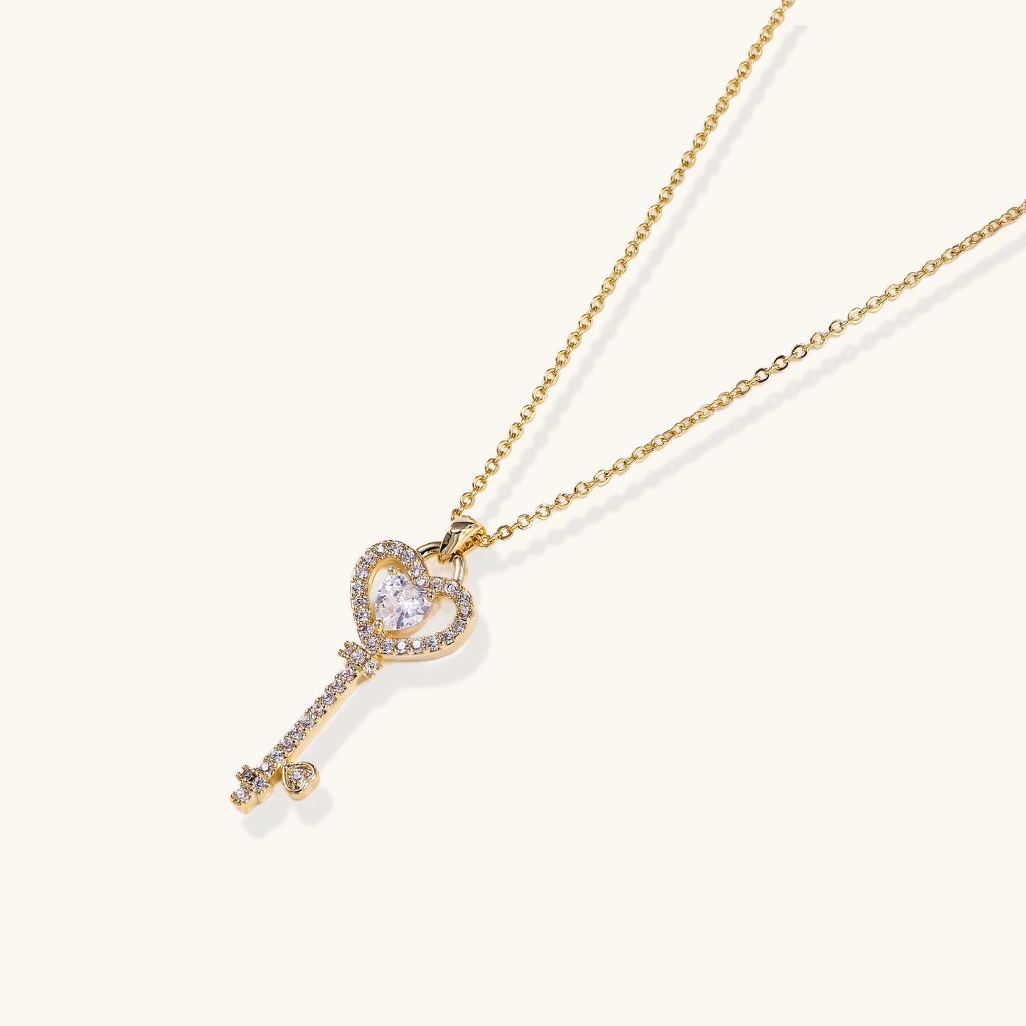 Gold-plated key pendant necklace with heart top and crystal embellishments on adjustable chain against cream background