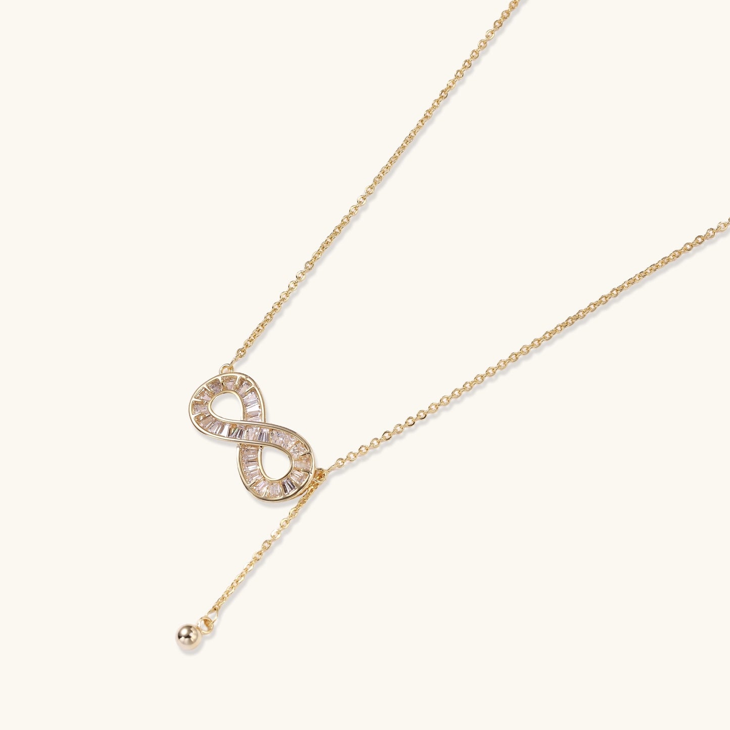 Delicate 14K gold plated infinity pendant with crystal accents on adjustable chain with small ball charm detail.