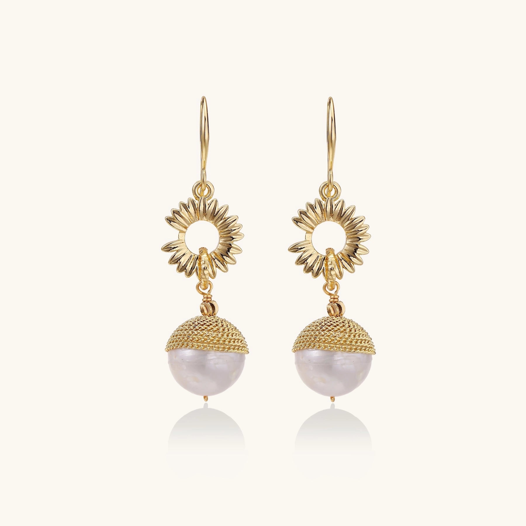 Gold-plated sunburst flower earrings with baroque pearl drops and textured metal caps on neutral background.