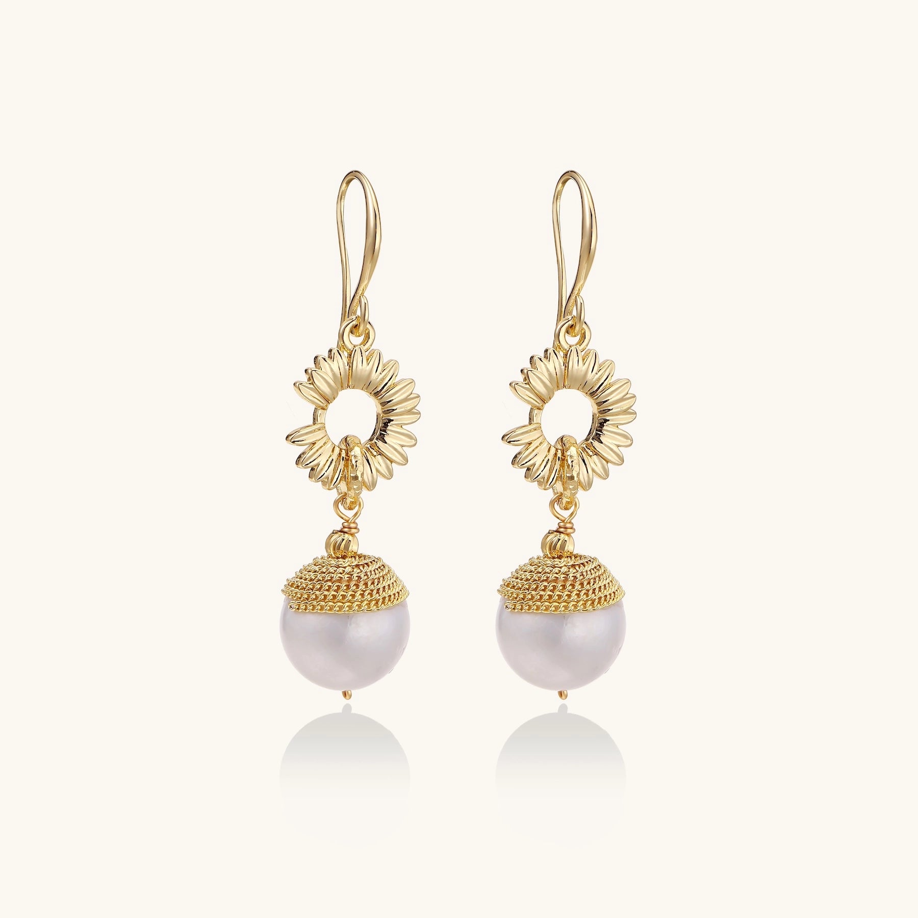 Gold-plated sunburst flower earrings with baroque pearl drops and textured metal caps on neutral background.