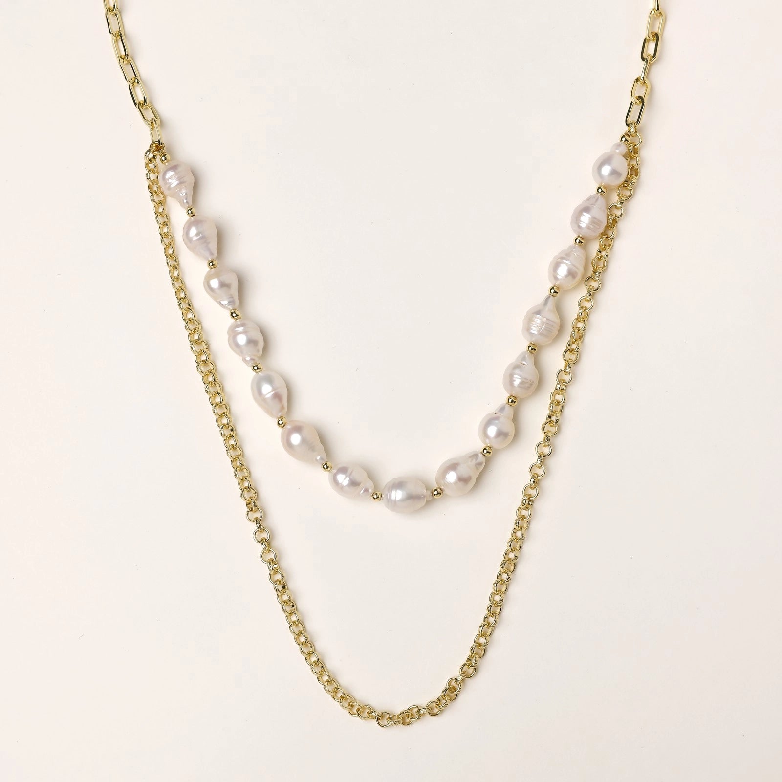 Layered gold chain necklace with irregular freshwater pearls on cream background, showing adjustable dual-strand design.