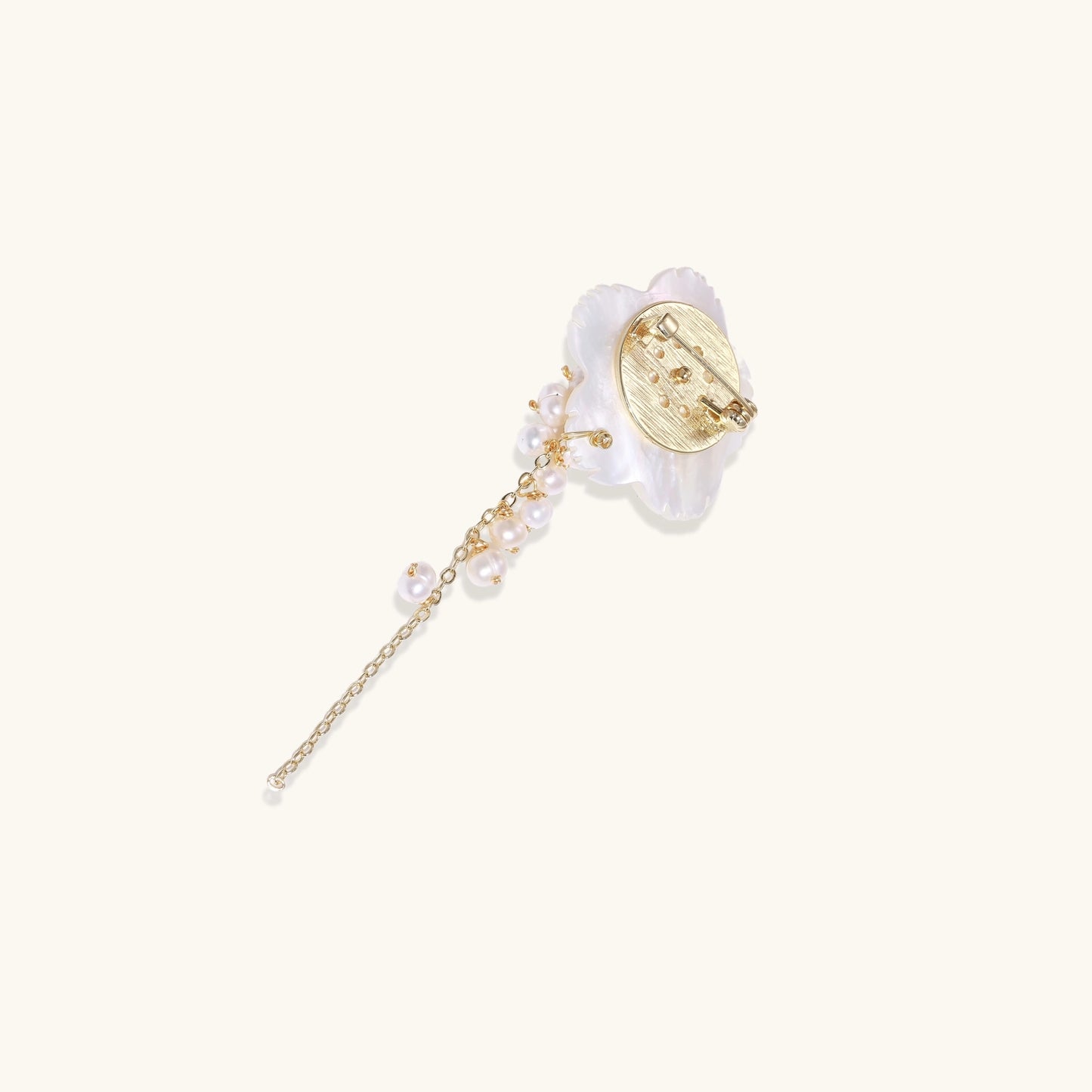 Delicate hair pin featuring translucent shell flower with cascading freshwater pearls on gold chain against cream background.