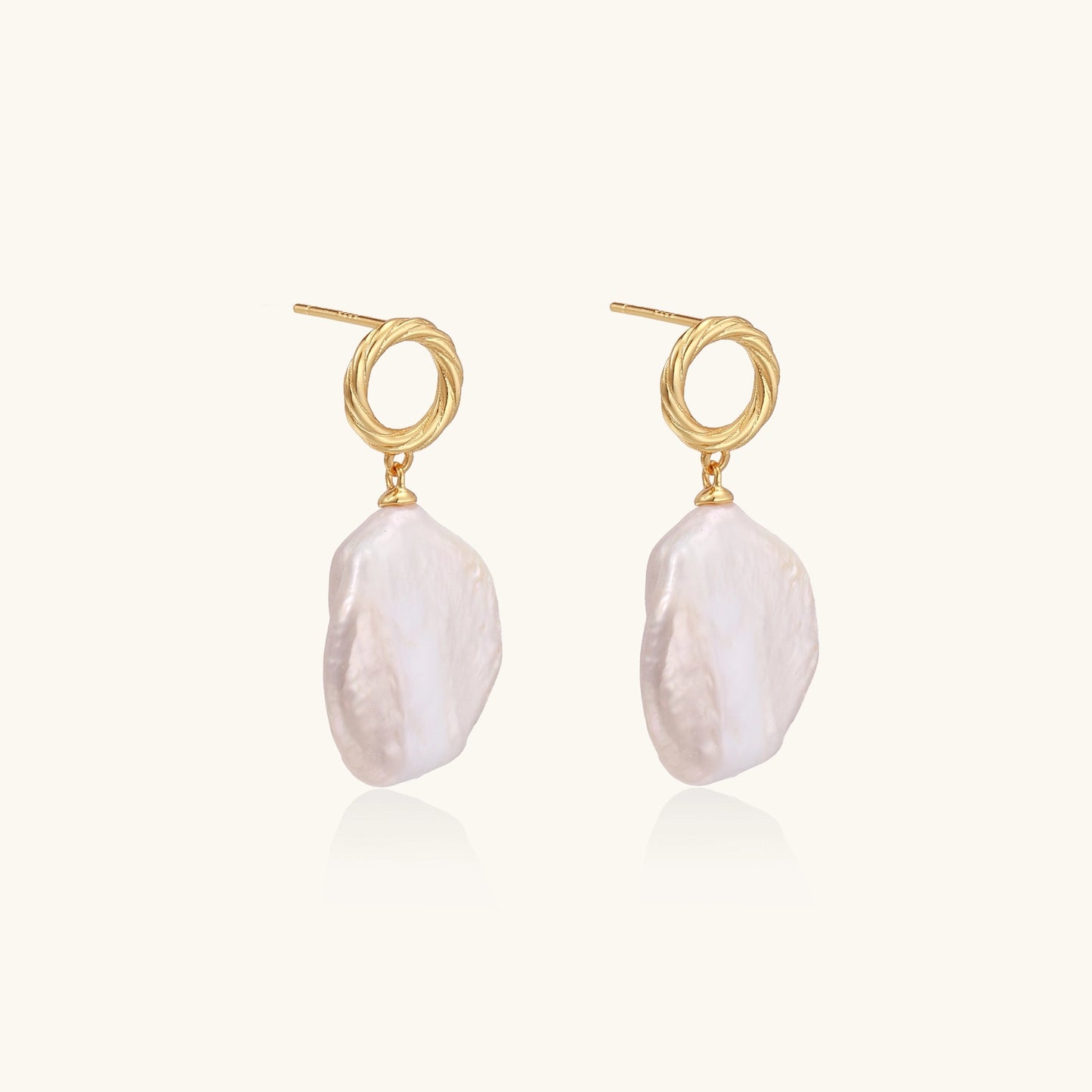Gold-plated twisted stud earrings with large blush baroque pearls hanging elegantly on white background.