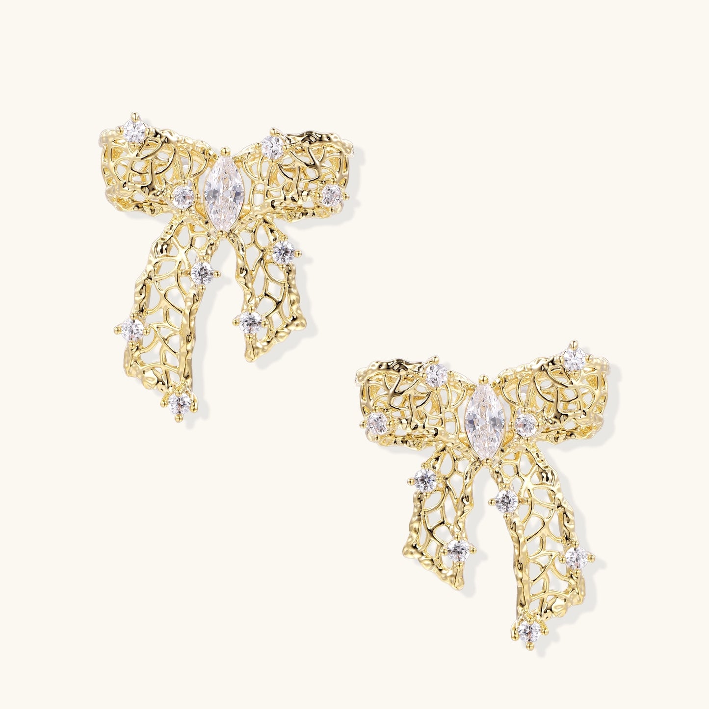 Gold and silver bow-shaped earrings with intricate lattice pattern and clear zirconia stones on neutral background.