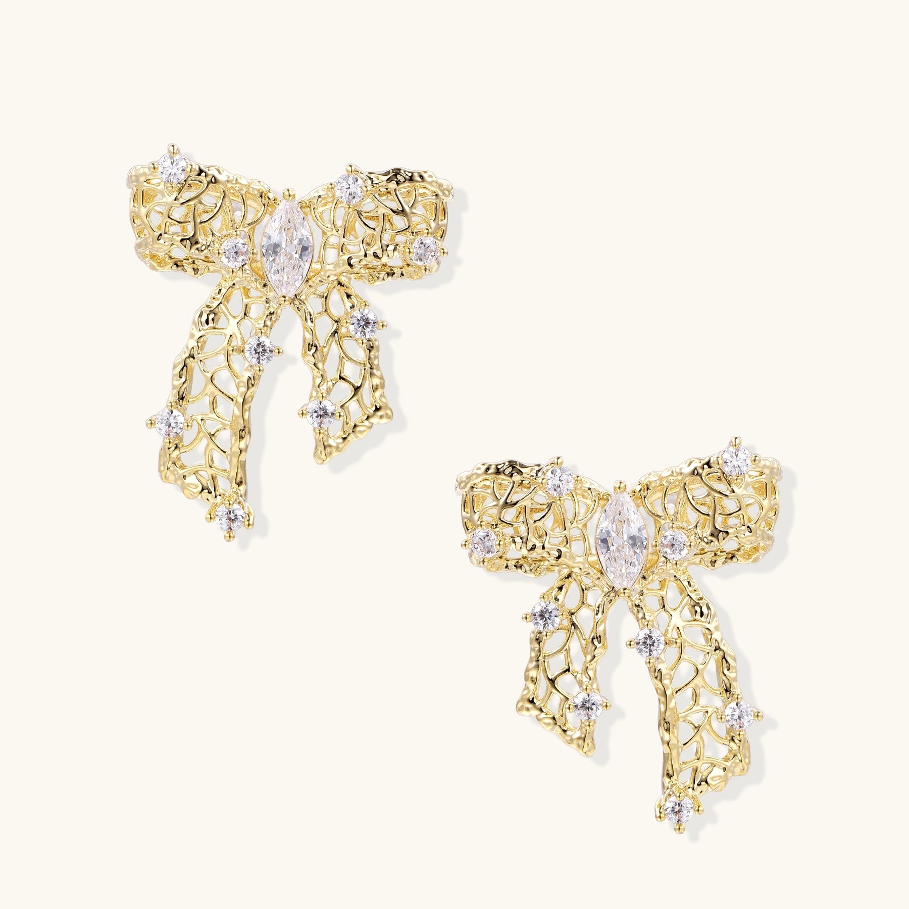 Gold and silver bow-shaped earrings with intricate lattice pattern and clear zirconia stones on neutral background.