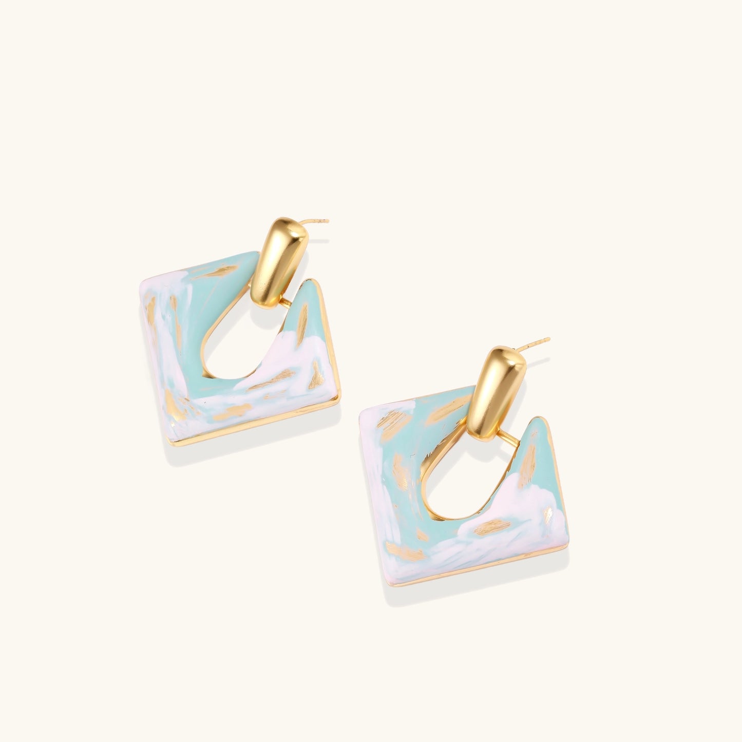 Diamond-shaped gold-plated earrings with pastel marble enamel in turquoise and lavender swirls on beige background