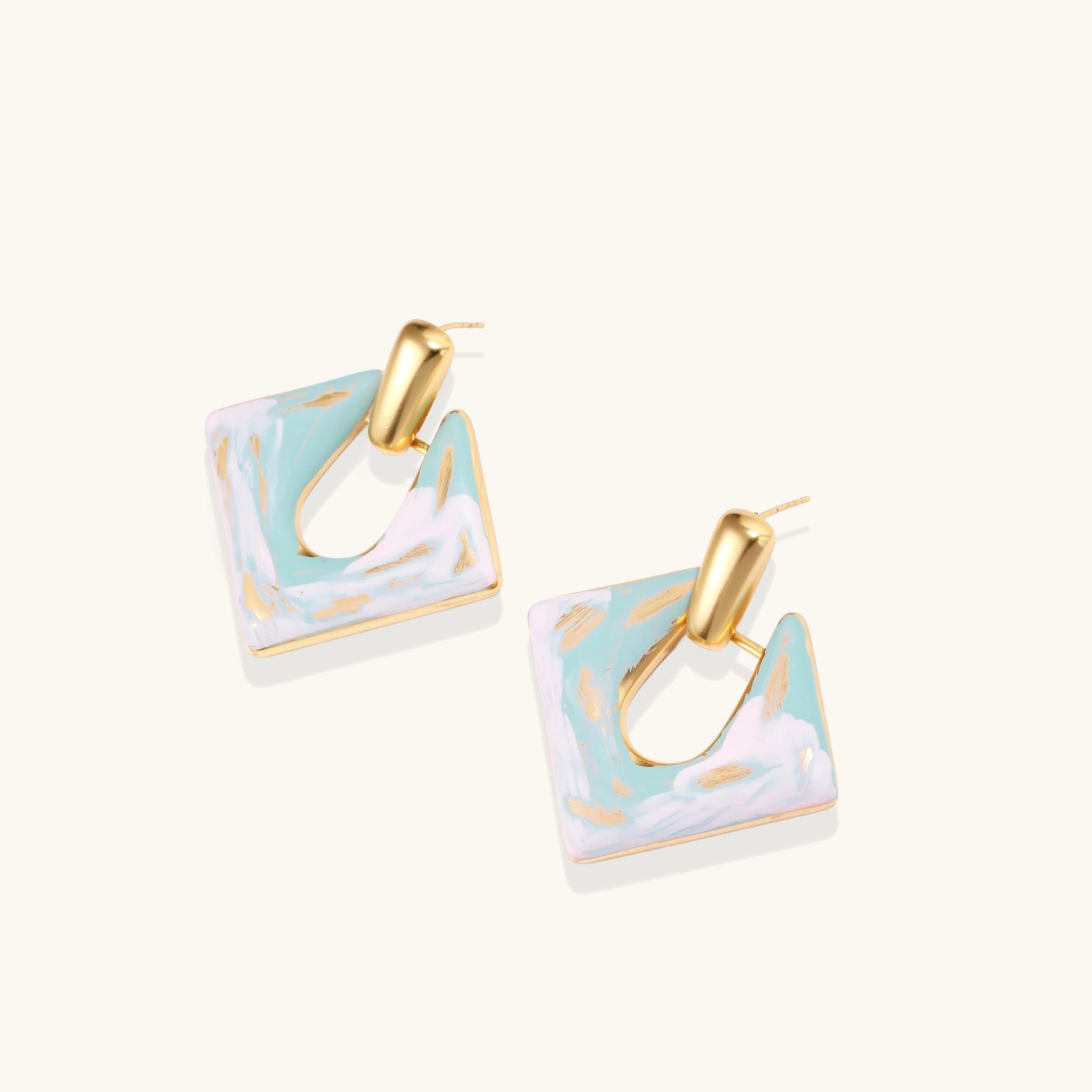 Diamond-shaped gold-plated earrings with pastel marble enamel in turquoise and lavender swirls on beige background