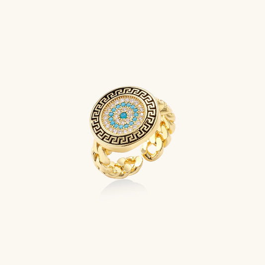 Gold-plated brass ring with Greek key border, evil eye center, and turquoise cubic zirconia stones in chunky chain band style.