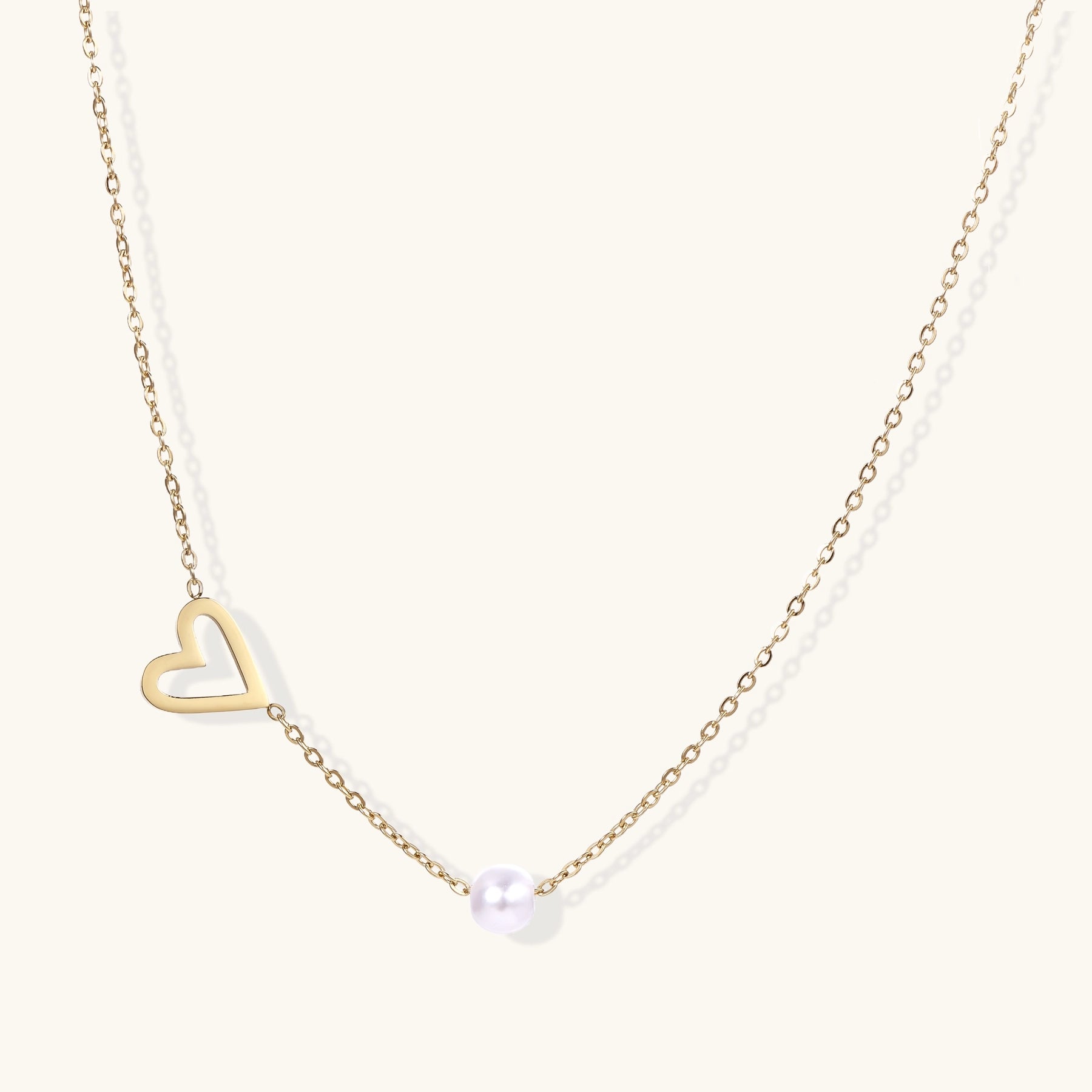 Dainty 14K gold-plated necklace with open heart pendant and white pearl bead on neutral background