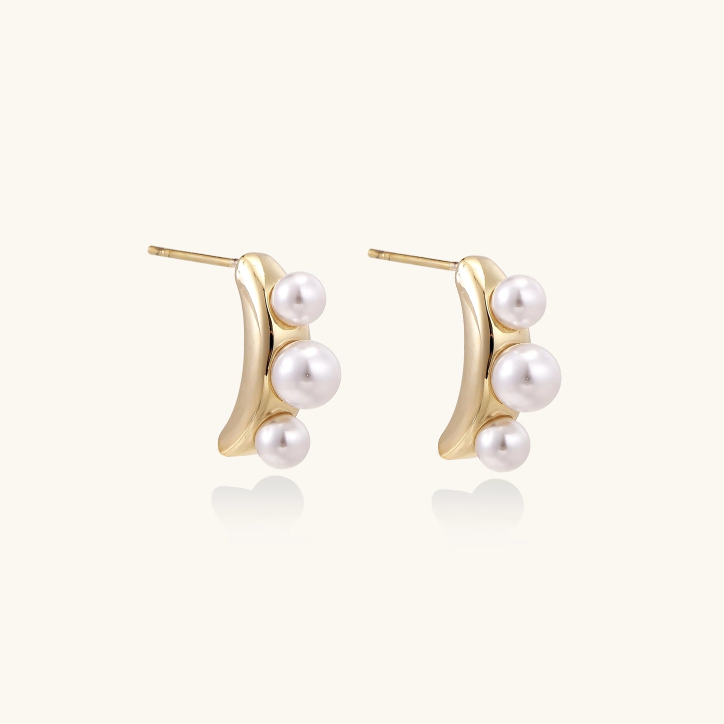 Delicate gold stud earrings with three lustrous white freshwater pearls arranged in an organic curved line.