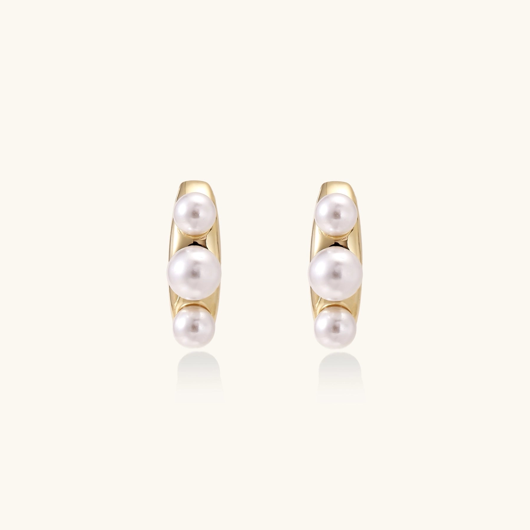 Delicate gold stud earrings with three lustrous white freshwater pearls arranged in an organic curved line.