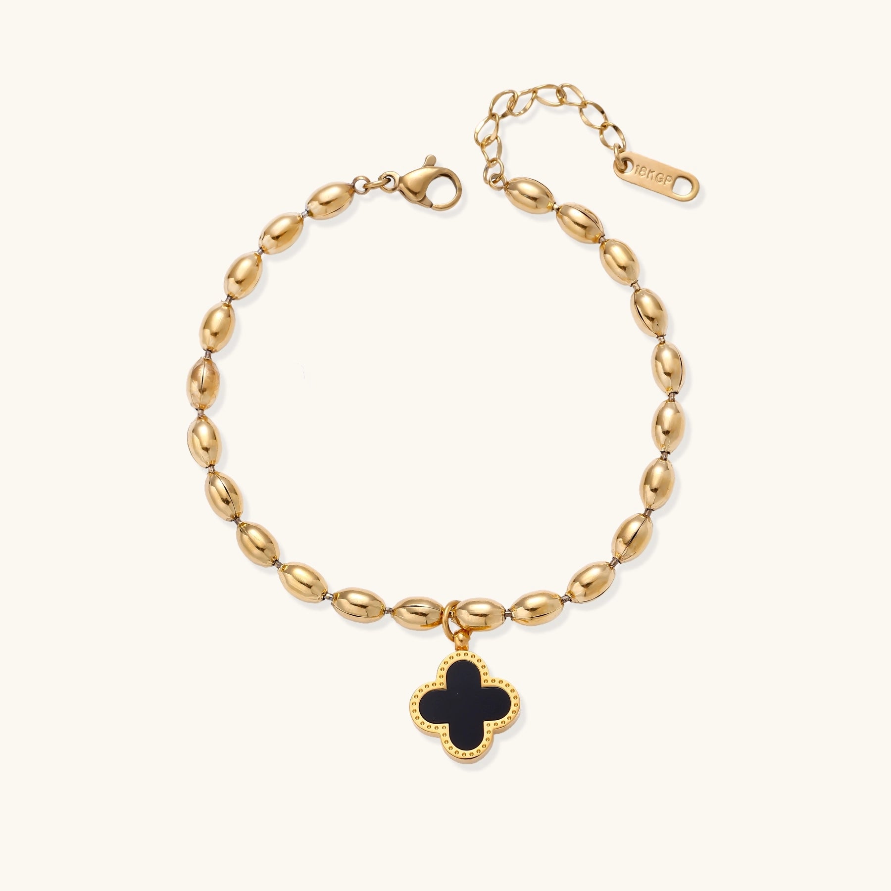 Dainty gold-plated beaded bracelet with oval links and four-leaf clover charm pendant on neutral background.